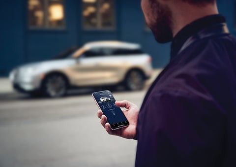 A person is shown interacting with a smartphone to connect to a Lincoln vehicle across the street. | Capital Lincoln of Wilmington in Wilmington NC
