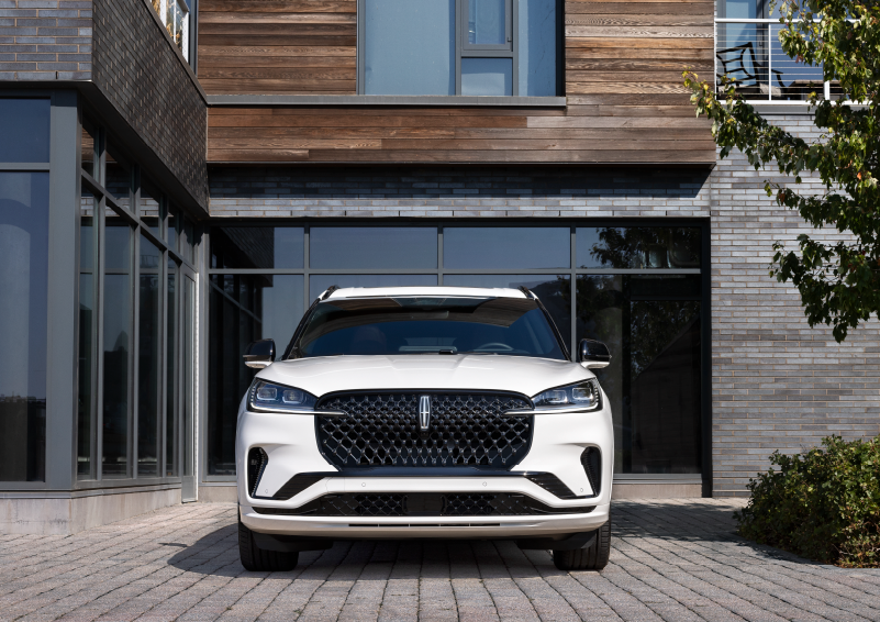 A white 2025 Lincoln Aviator® SUV is shown parked outside a modern building with gray brick and wood accents. | Capital Lincoln of Wilmington in Wilmington NC