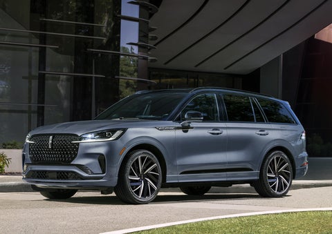 A gray 2025 Lincoln Aviator® SUV is parked outside a modern building showcasing the driver’s side of the vehicle. | Capital Lincoln of Wilmington in Wilmington NC