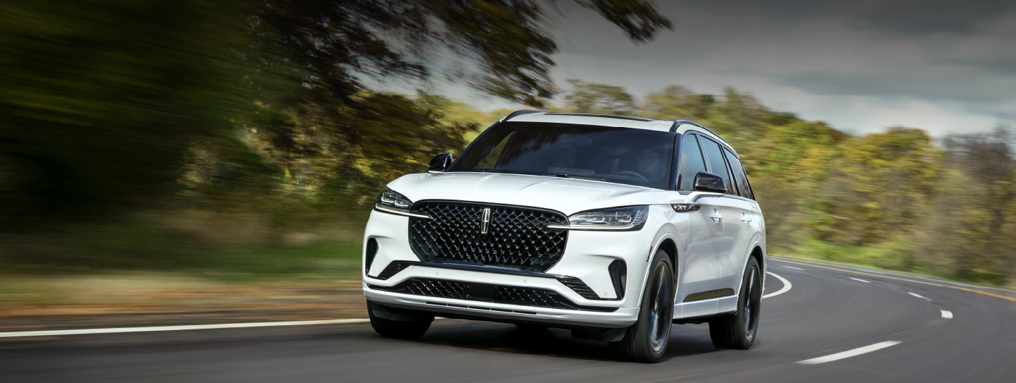 A white 2025 Lincoln Aviator® SUV is being driven down a road lined with trees. | Capital Lincoln of Wilmington in Wilmington NC