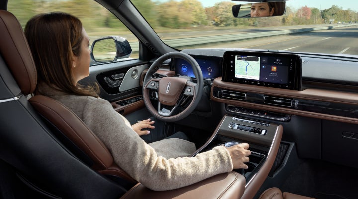 A 2026 Lincoln Aviator® SUV is being driven hands-free on a highway near a forest | Capital Lincoln of Wilmington in Wilmington NC