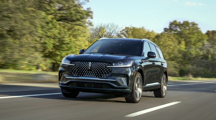 A 2026 Lincoln Black Label™ Aviator® SUV is being driven down a road lined with trees. | Capital Lincoln of Wilmington in Wilmington NC