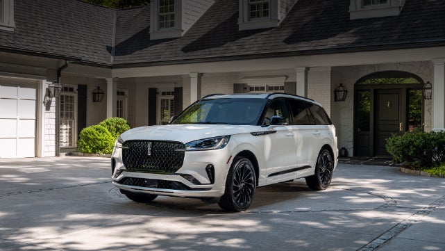 A white 2026 Lincoln Aviator® SUV is parked in the driveway of a luxury home. | Capital Lincoln of Wilmington in Wilmington NC