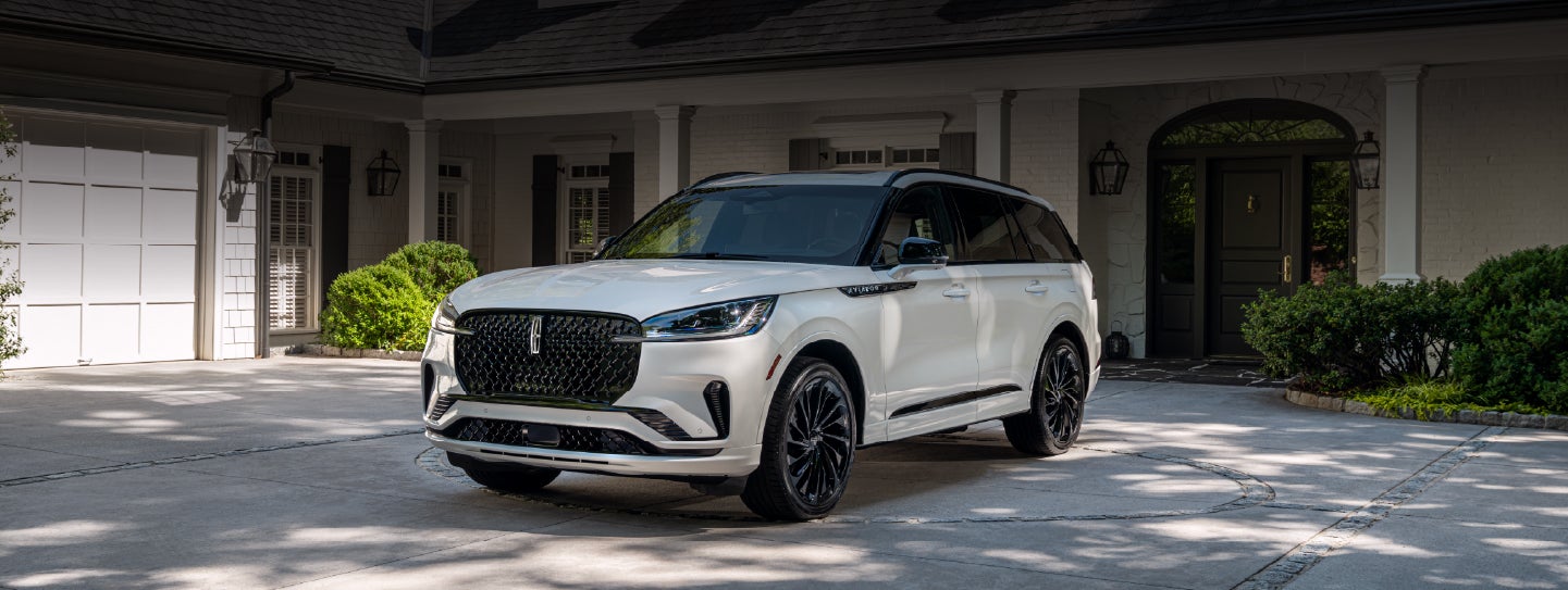 A white 2026 Lincoln Aviator® SUV is parked in the driveway of a luxury home. | Capital Lincoln of Wilmington in Wilmington NC