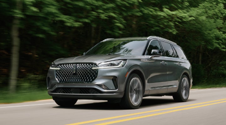 A 2027 Lincoln Aviator® SUV is being driven down a road lined with trees. | Capital Lincoln of Wilmington in Wilmington NC
