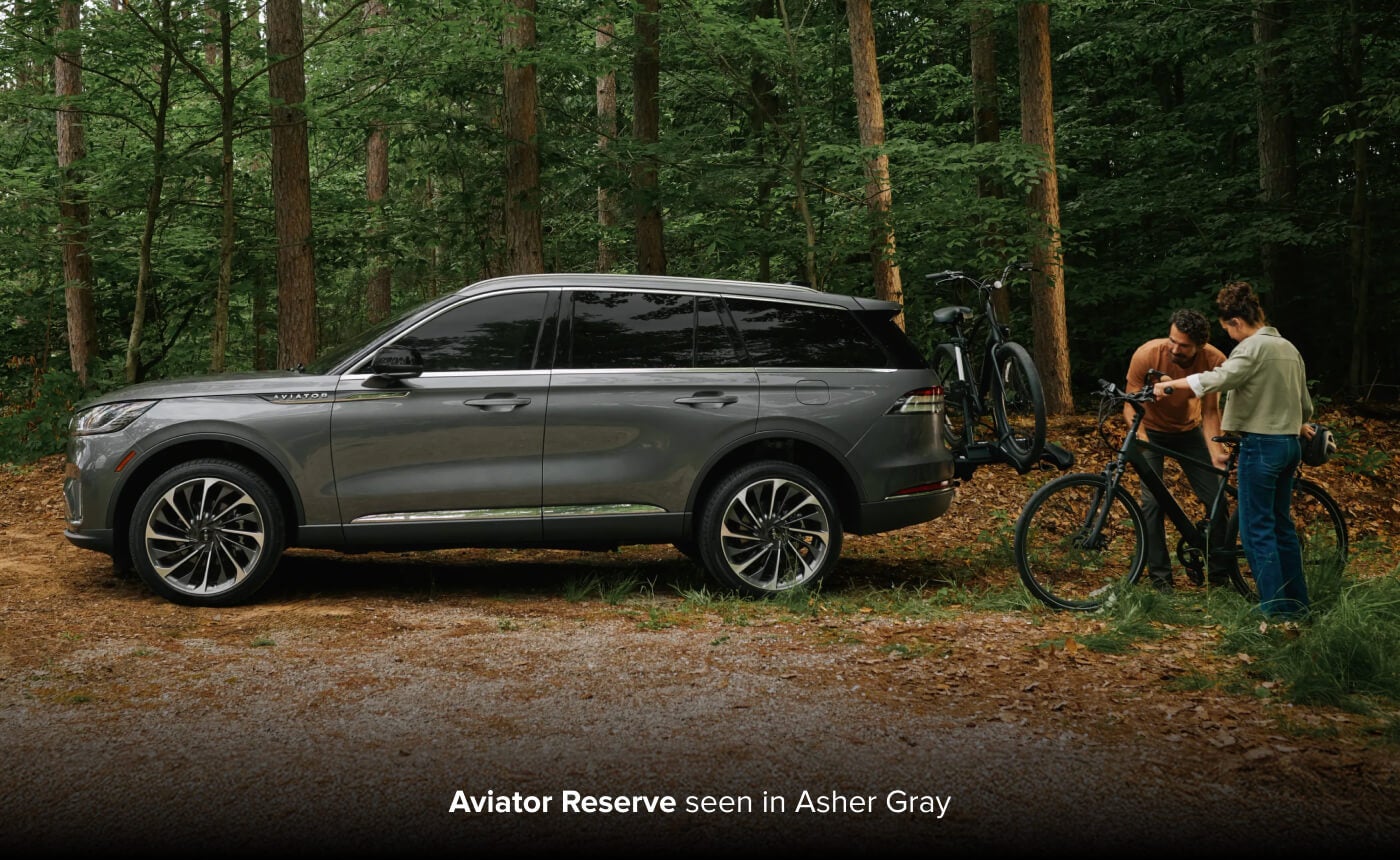 2027 Lincoln Aviator Reserve in Asher Gray parked in a forest as two people prepare bicycles beside the SUV.