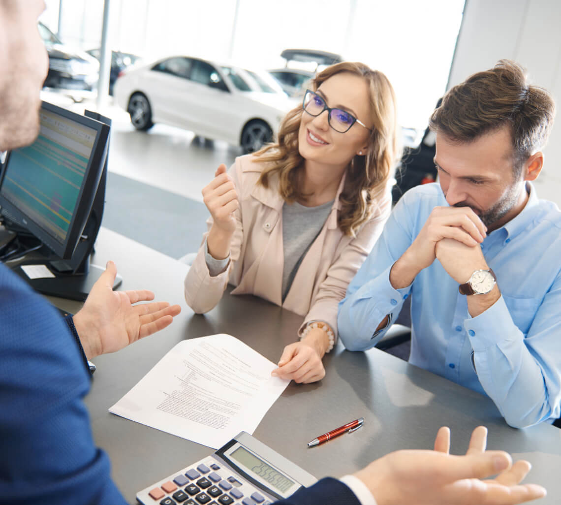 A couple discusses paperwork with an auto dealer sales rep.