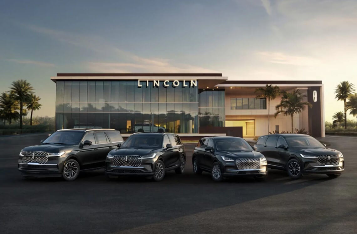A lineup of 2026 Lincoln vehicles parked in front of a modern Lincoln dealership at dusk.