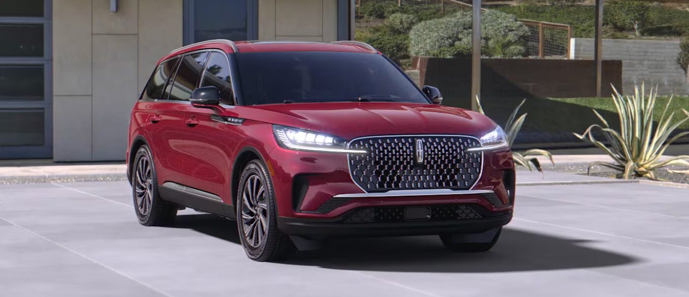 Exterior front three-quarter view of a red 2027 Lincoln Aviator parked in the driveway of an upscale home.