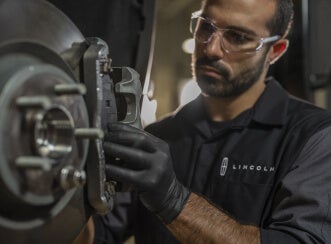 Close-up view of a certified Lincoln service technician in protective safety glasses inspecting a front brake rotor assembly.