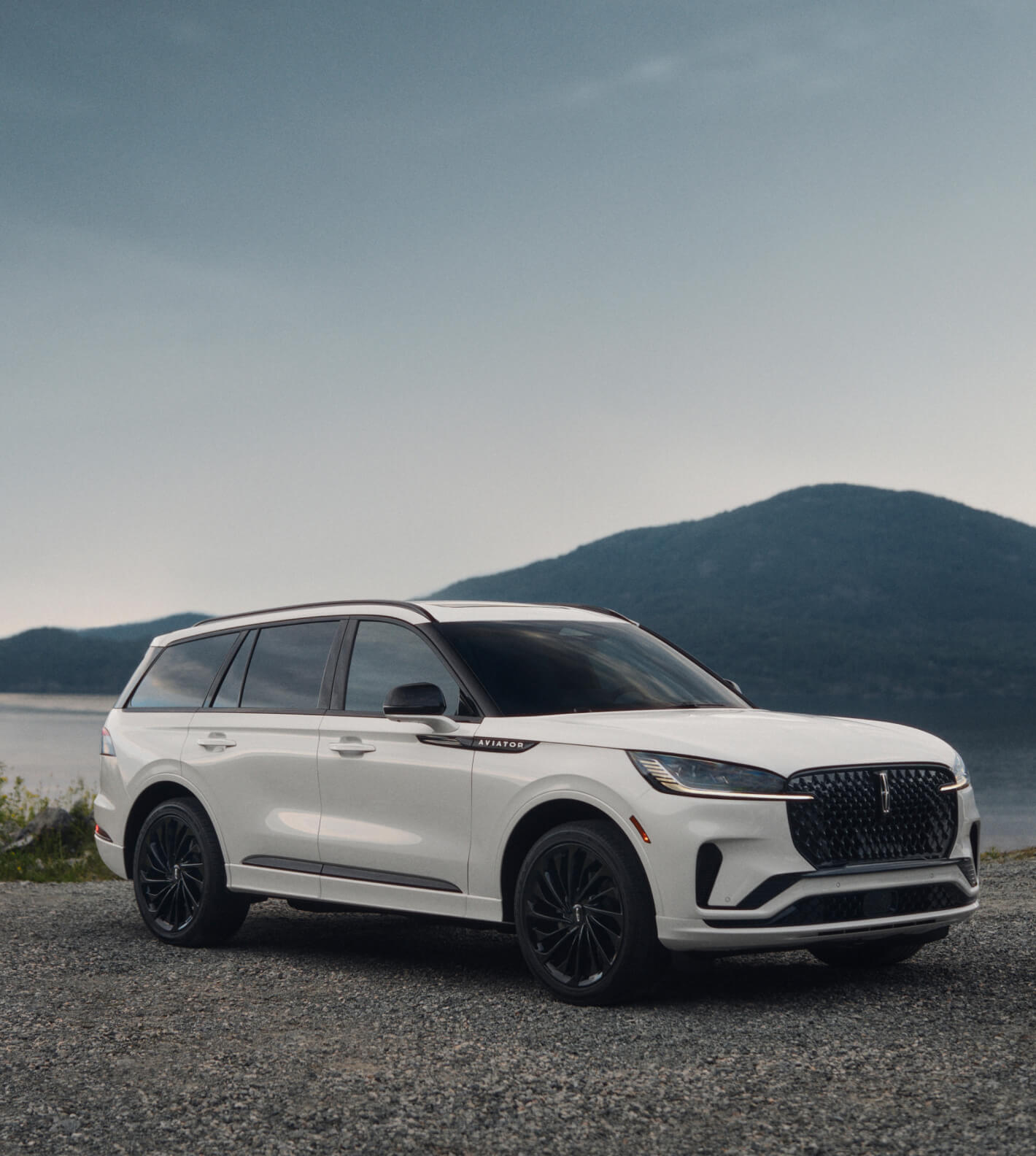 Front three-quarter view of a white Lincoln Aviator parked near a mountain lake.