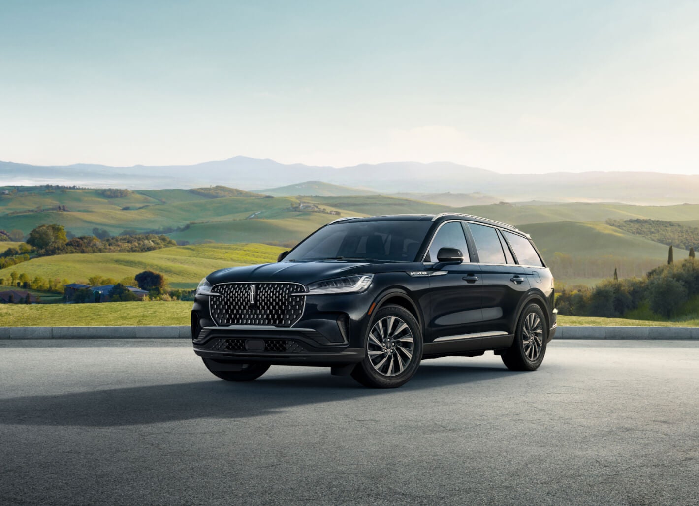 Front three-quarter view of a black Lincoln Aviator overlooking rolling green hills.