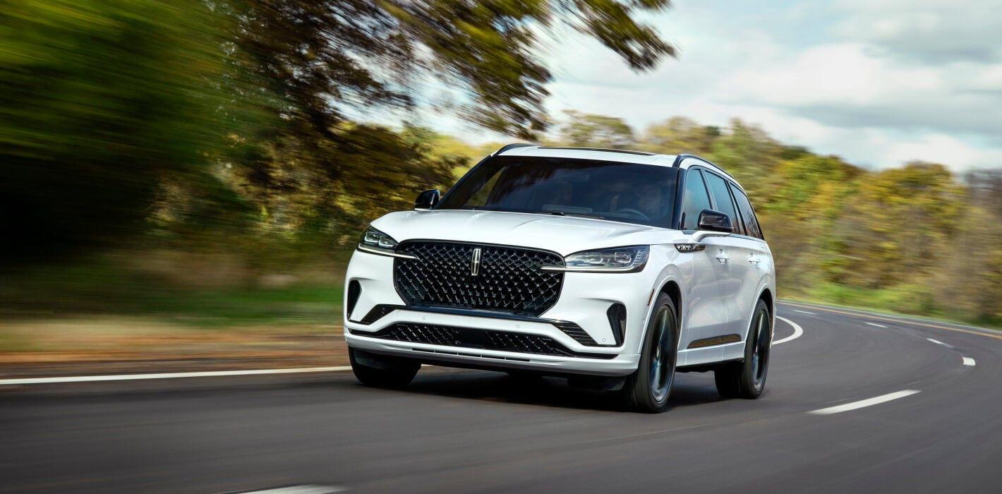 Front three-quarter view of a white Lincoln Aviator driving on a winding paved road.