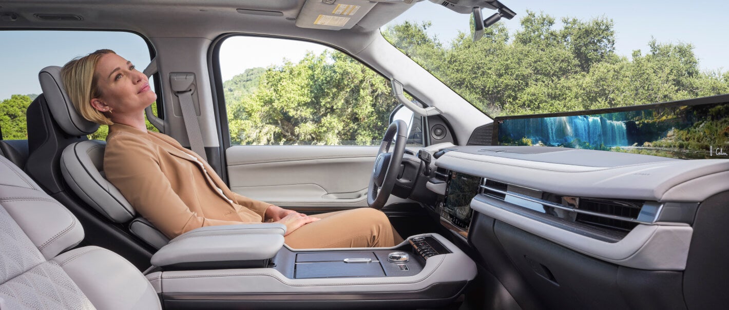 Wide side view of a passenger reclining in a 2026 Lincoln Navigator front driver seat with trees outside.